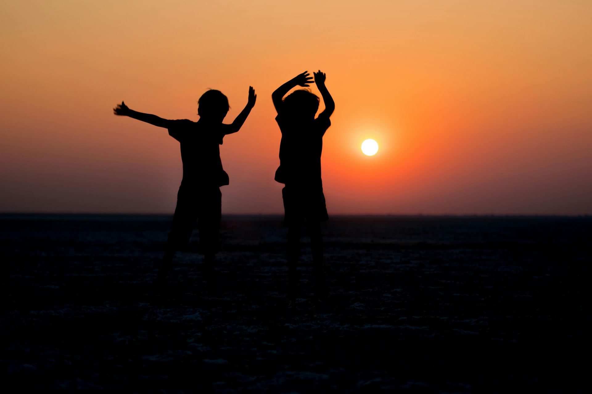 Two silhouetted children dance in front of a setting sun — Tewantin Medical Centre In Tewantin, QLD
