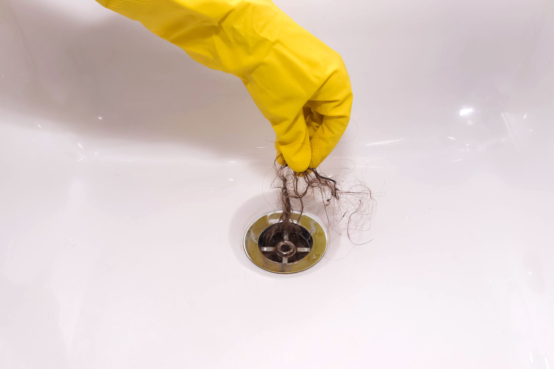 Gloved hand holding a clump of hair removed from a bathtub drain.