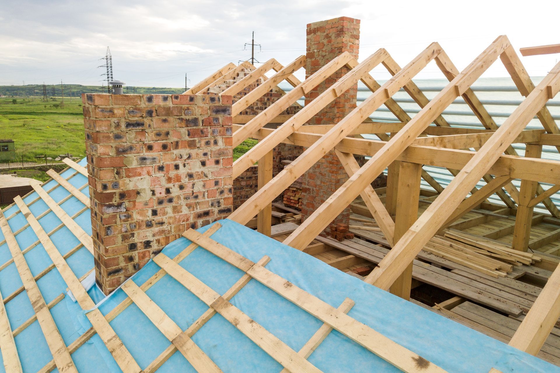 Roof construction: Wooden beams, brick chimney, and blue underlayment.
