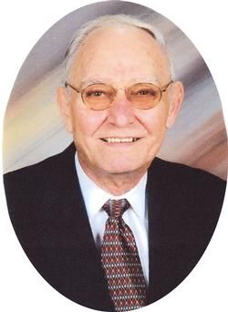 Portrait of an individual wearing glasses, a suit, and a tie, framed in an oval against a light, abstract background.