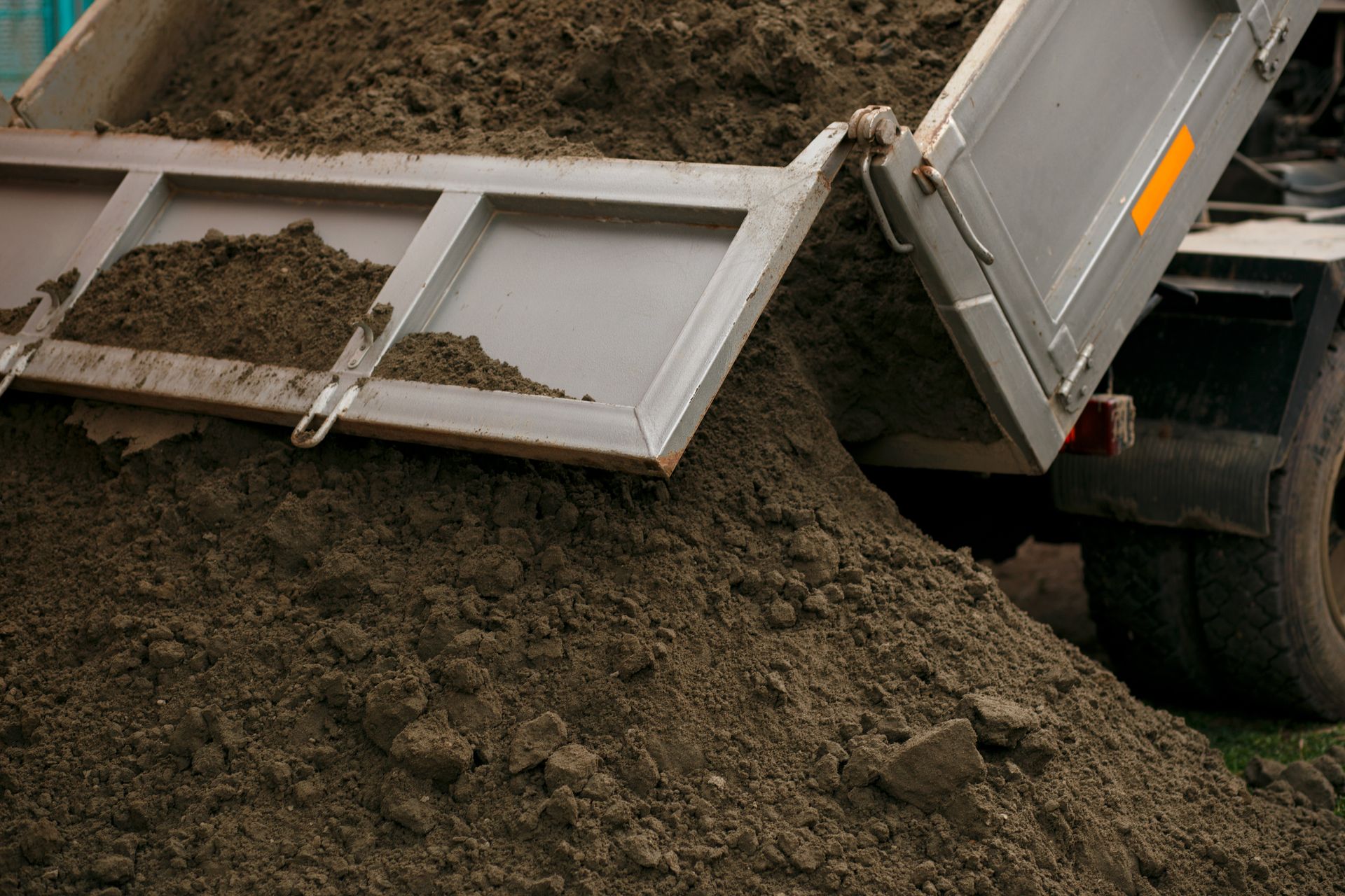 A dump truck is dumping dirt into a pile.