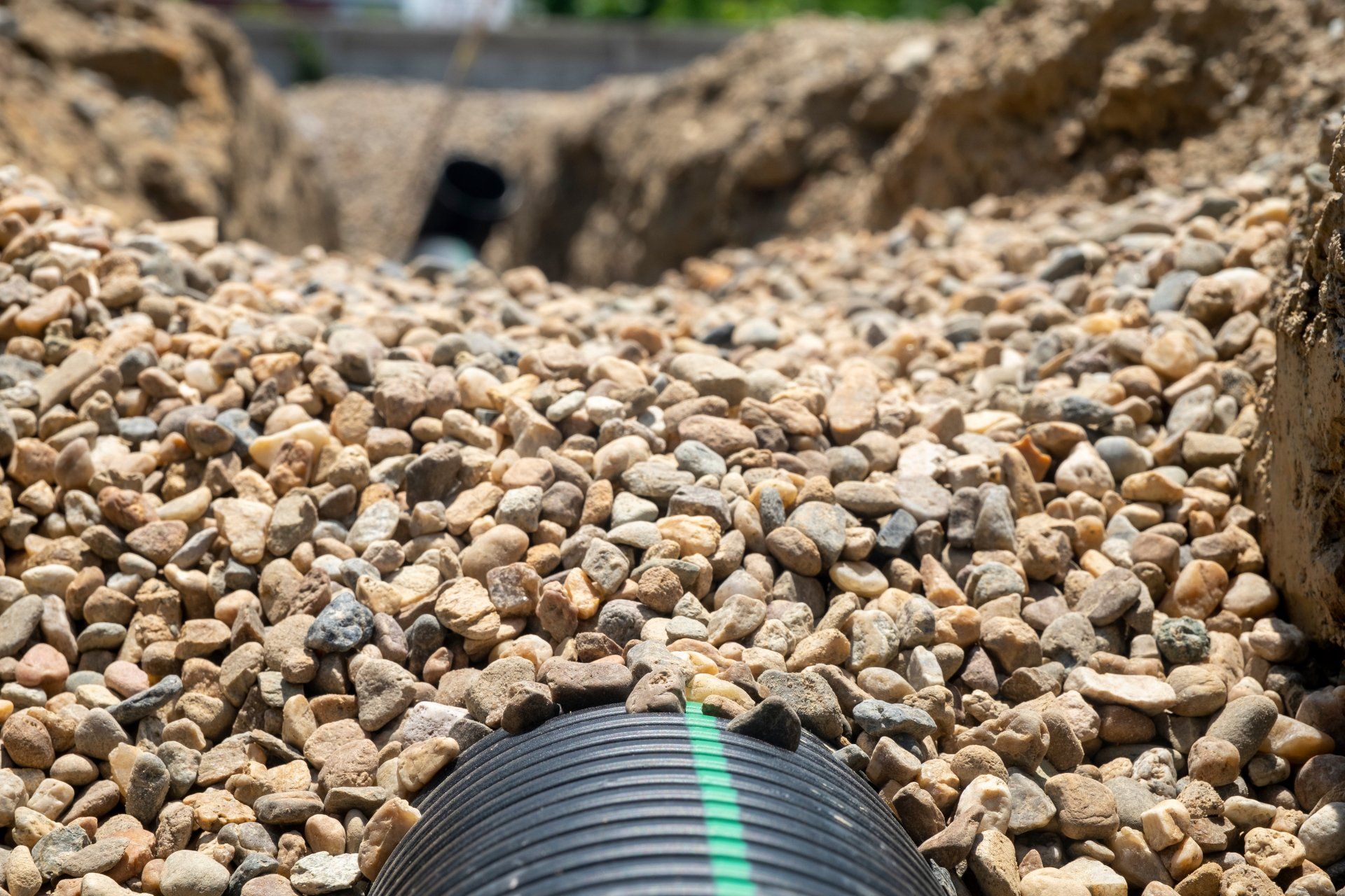 A black pipe is sitting on top of a pile of gravel.