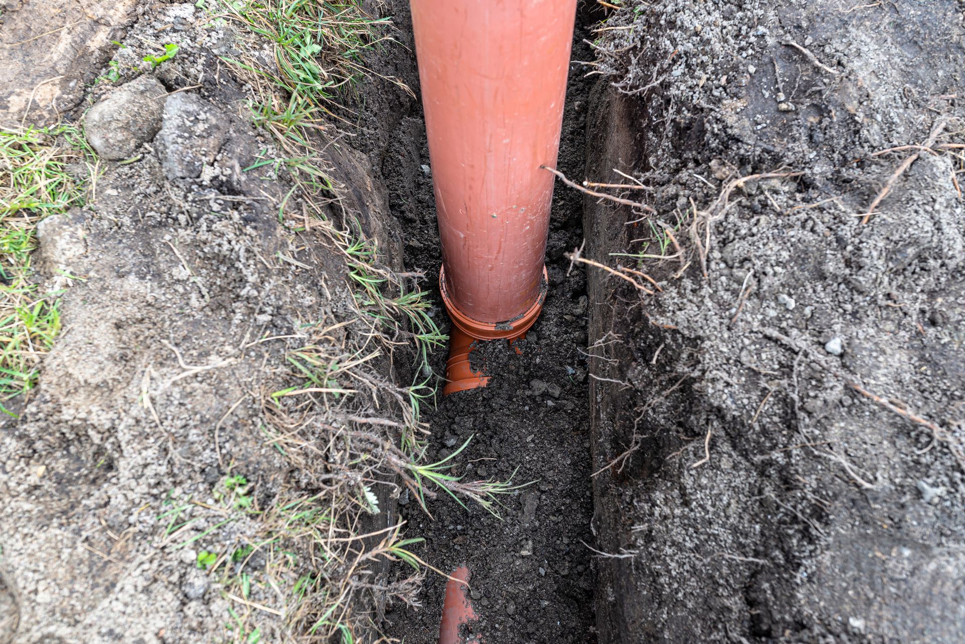 A red pipe is sitting in the dirt next to a grassy area.