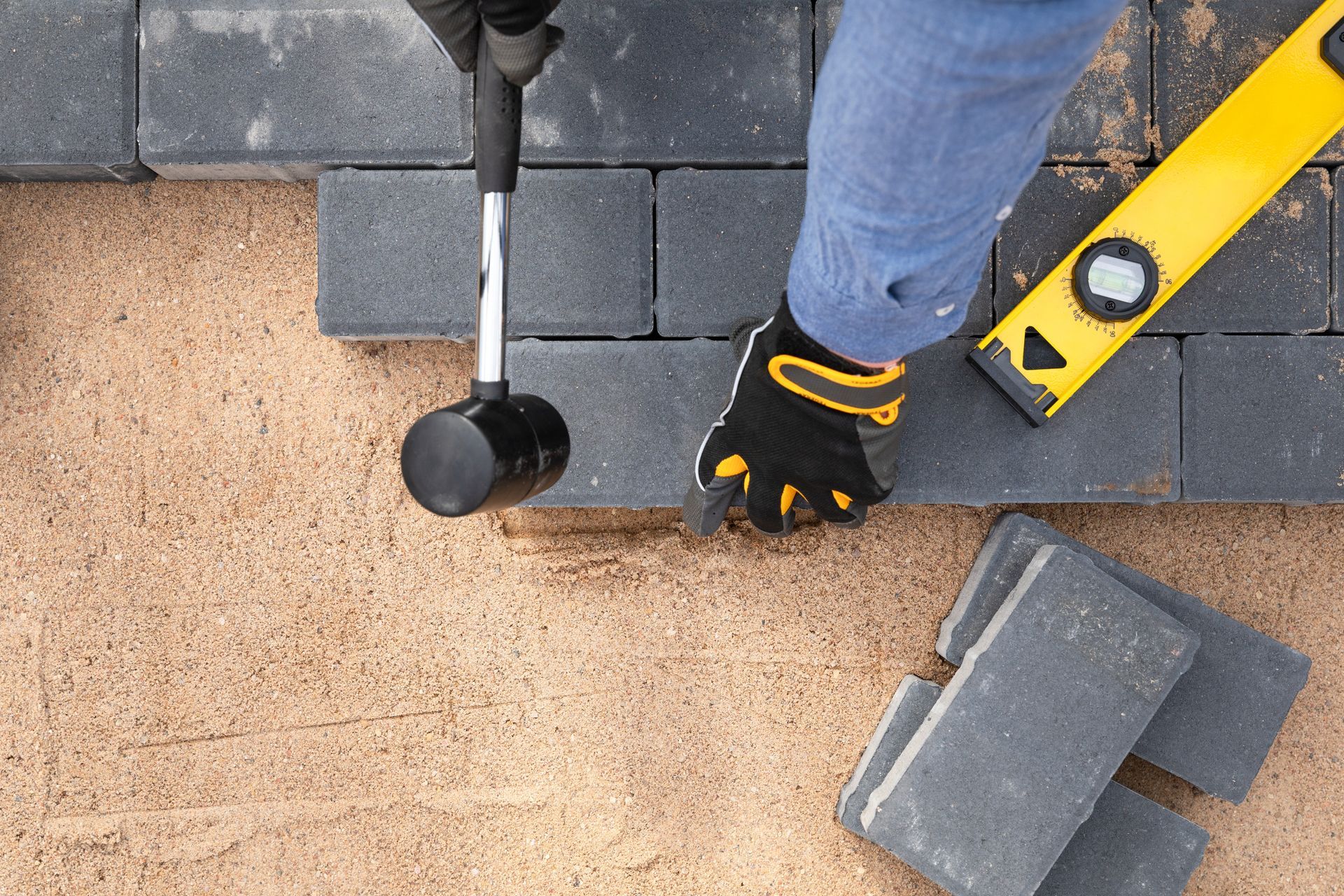 A person is laying bricks on the ground with a level and a hammer.