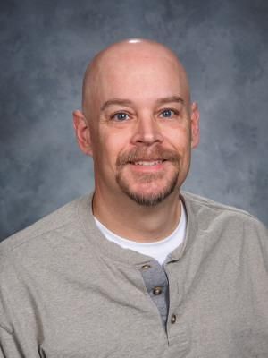 a bald man with a beard is wearing a grey shirt and smiling for the camera .