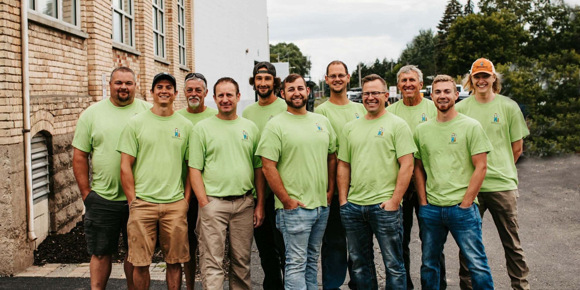 Group of people in matching green shirts standing outdoors beside a building, posing for a photo