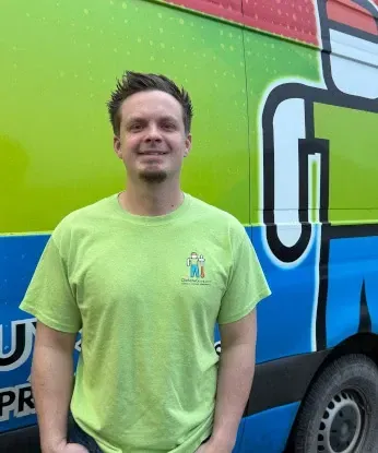 Smiling person in a lime green shirt standing in front of a colorful delivery truck