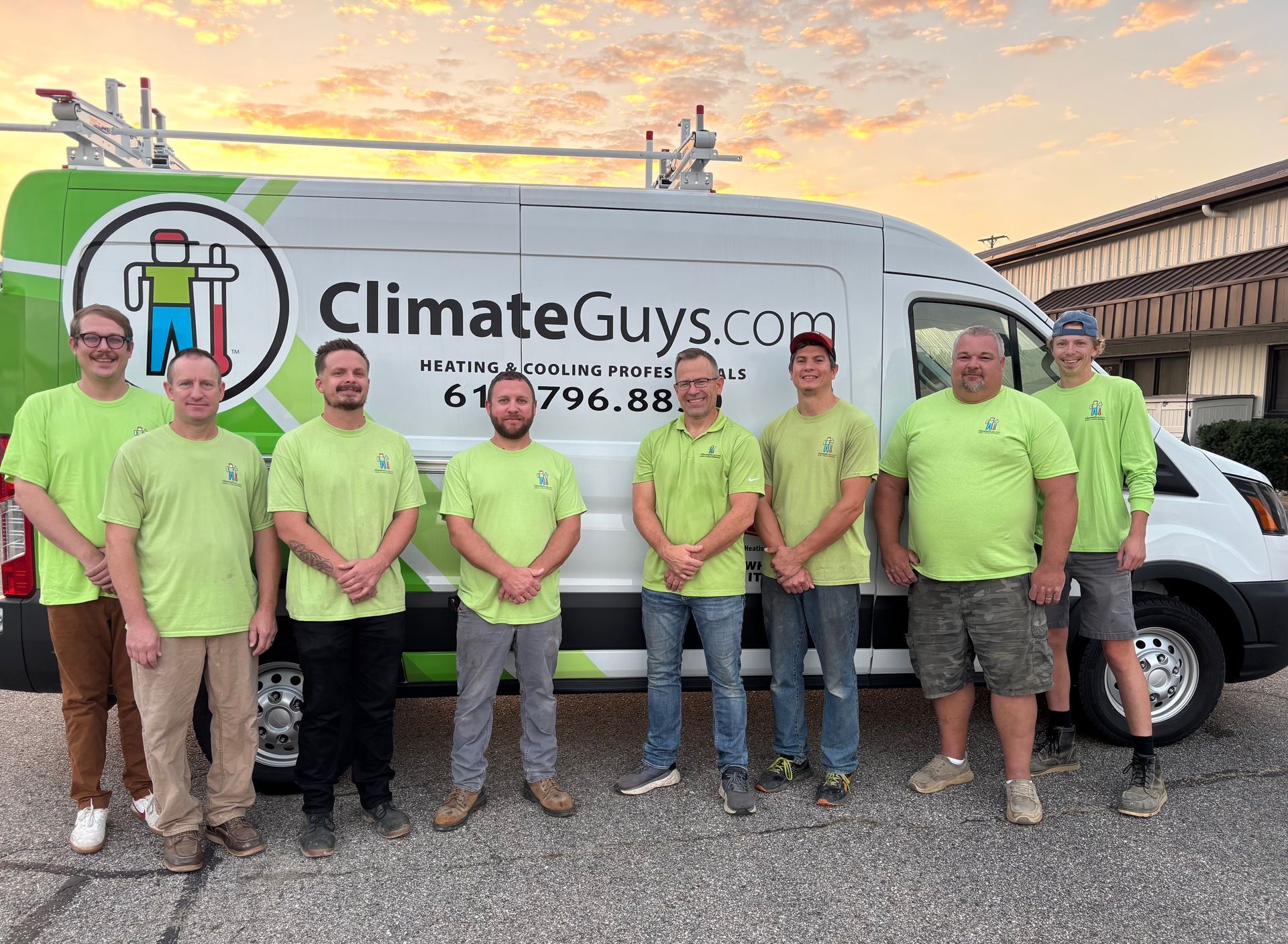 Group of people in matching green shirts standing outdoors beside a building, smiling at the camera.