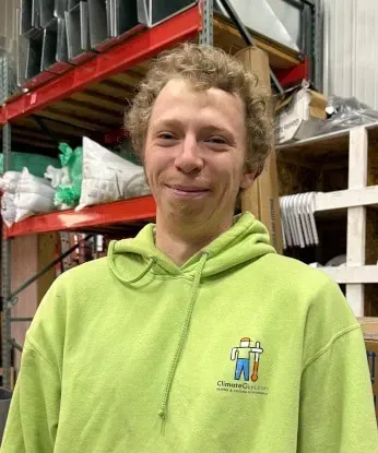 Person in a neon green hoodie smiling in a warehouse aisle with shelves and stacked supplies.
