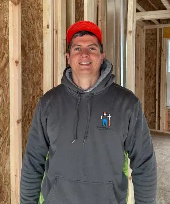 Smiling person in a red cap and gray hoodie standing inside a wood-framed construction site