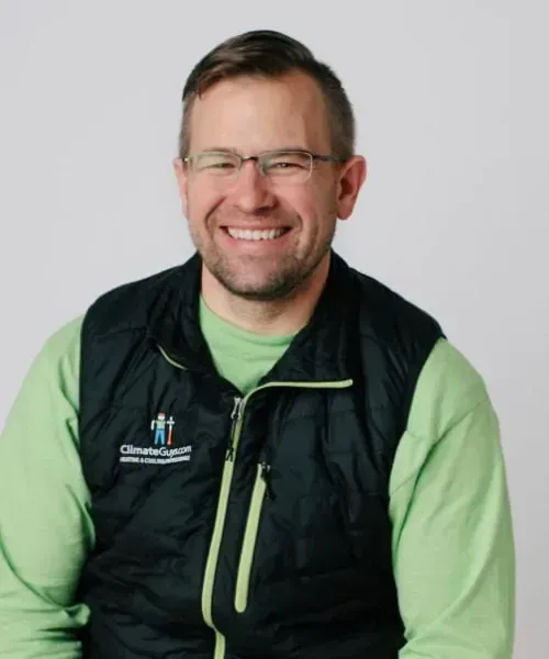 Smiling person in a black vest over a green shirt, seated against a light gray background