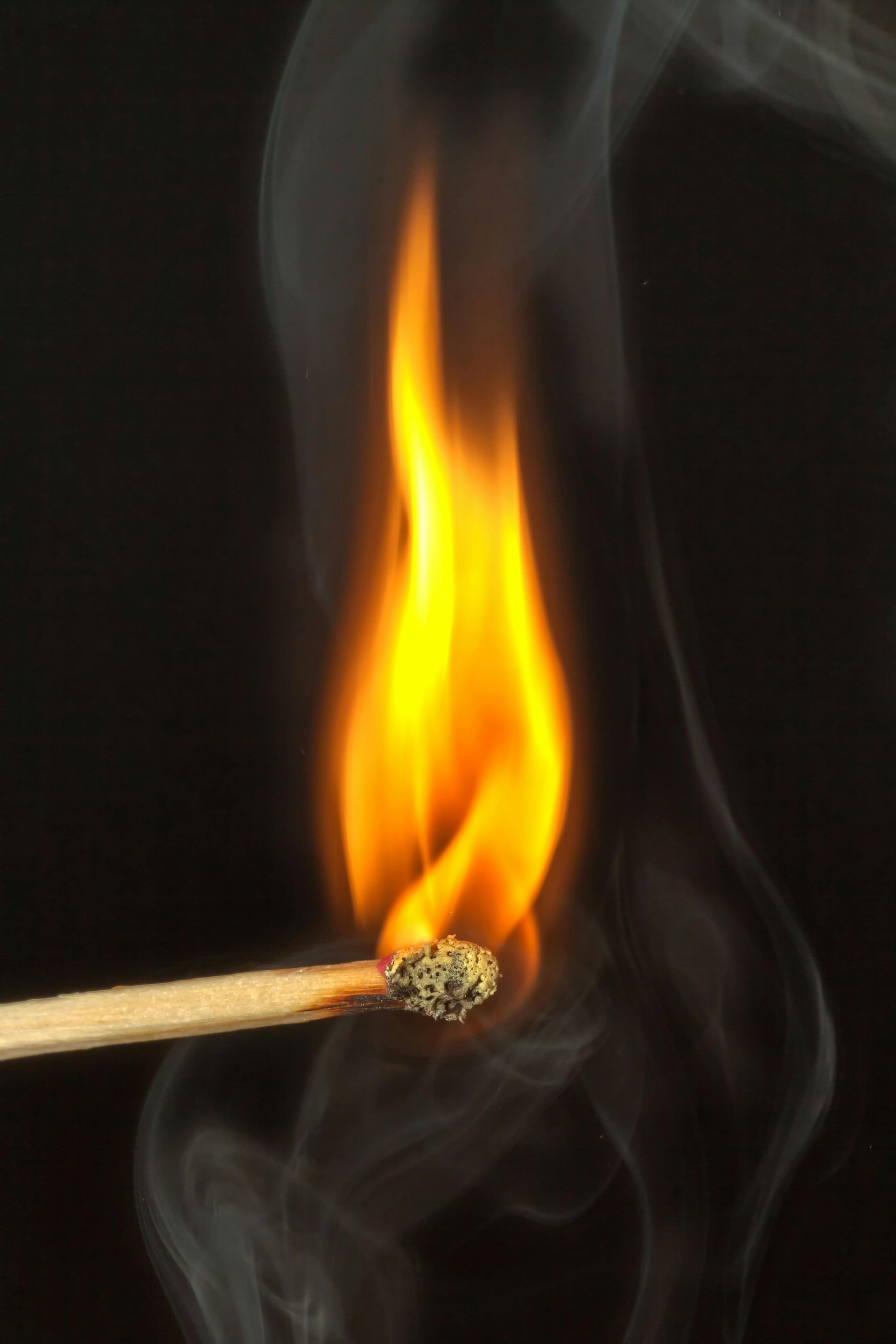 A lit match with a bright yellow-orange flame against a dark background.
