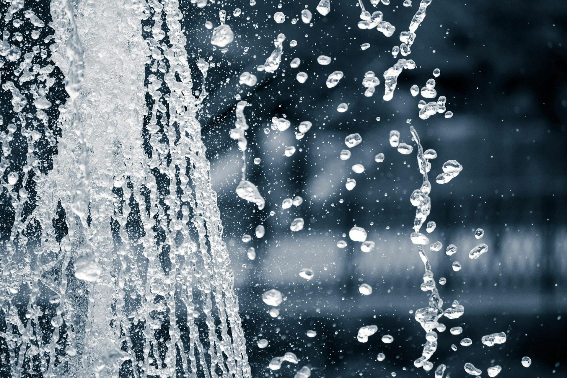 Water spraying from a fountain, with sparkling droplets against a dark background