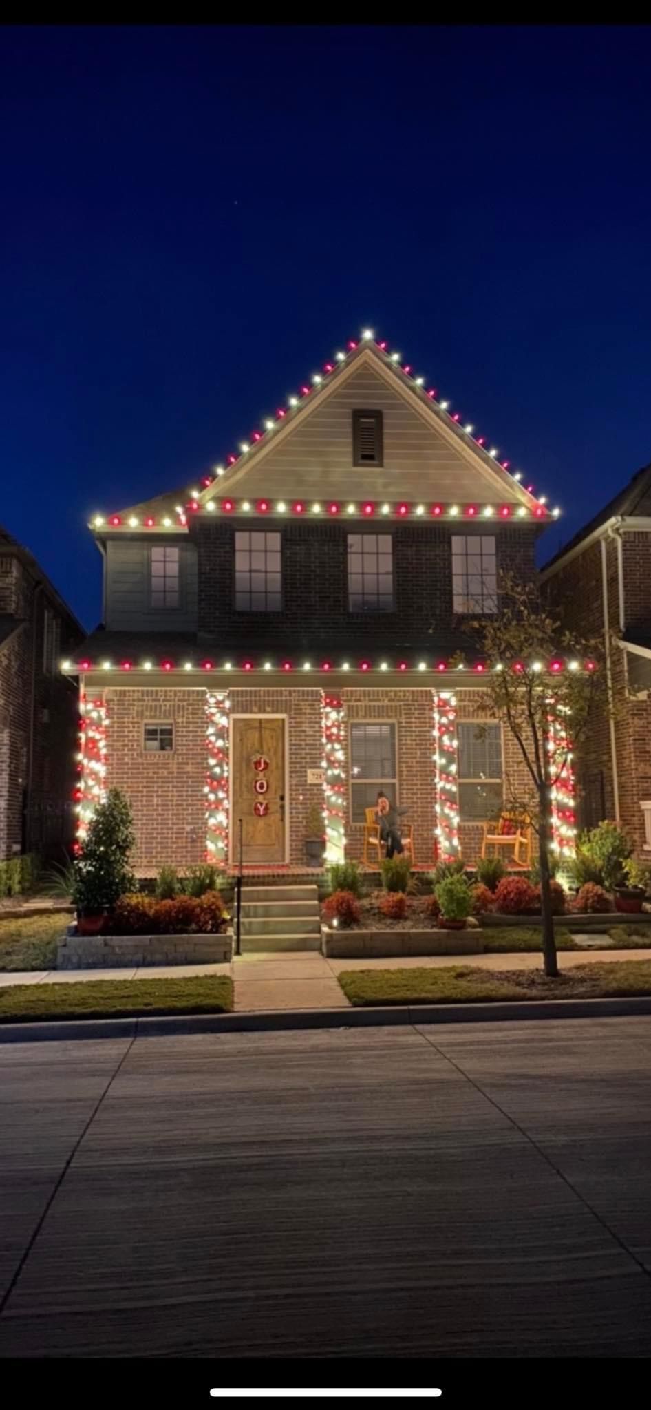 A two-story brick house at night, decorated with red and white candy cane-style Christmas lights on pillars and rooflines.