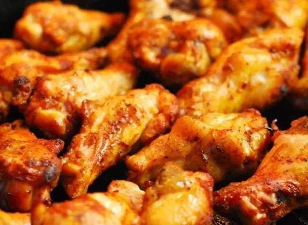 Primo piano di ali di pollo dorate, probabilmente fritte o al forno, ammucchiate su una superficie scura.