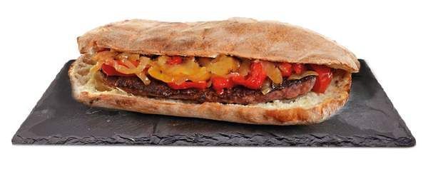 Panino su una lavagna grigio scuro con guarnizioni di peperoni e cipolle.