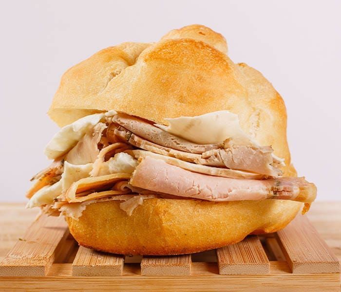 Panino su un vassoio di legno, con strati di carne e formaggio in un panino morbido.
