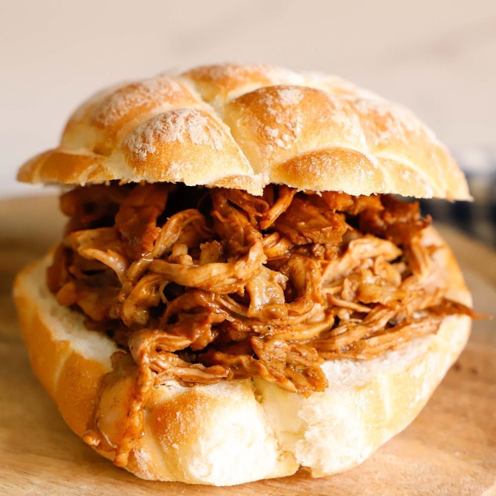 Panino con maiale sfilacciato, disposto su un panino rotondo e disposto su una superficie di legno.