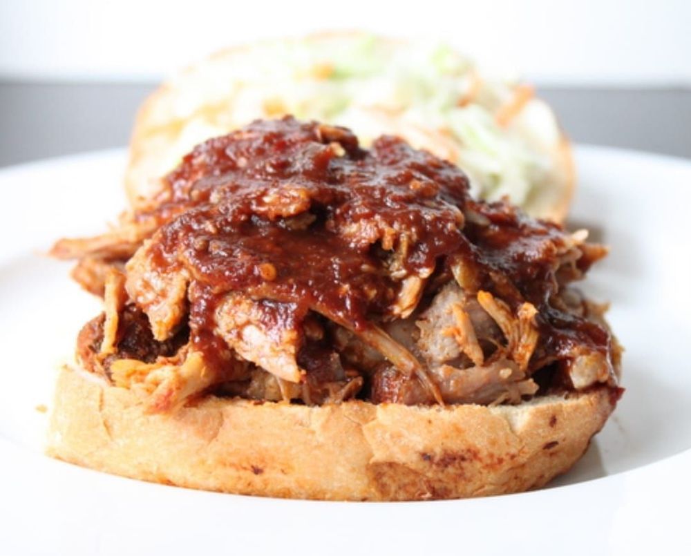 Panino con maiale sfilacciato su un panino tostato, condito con salsa barbecue e insalata di cavolo.