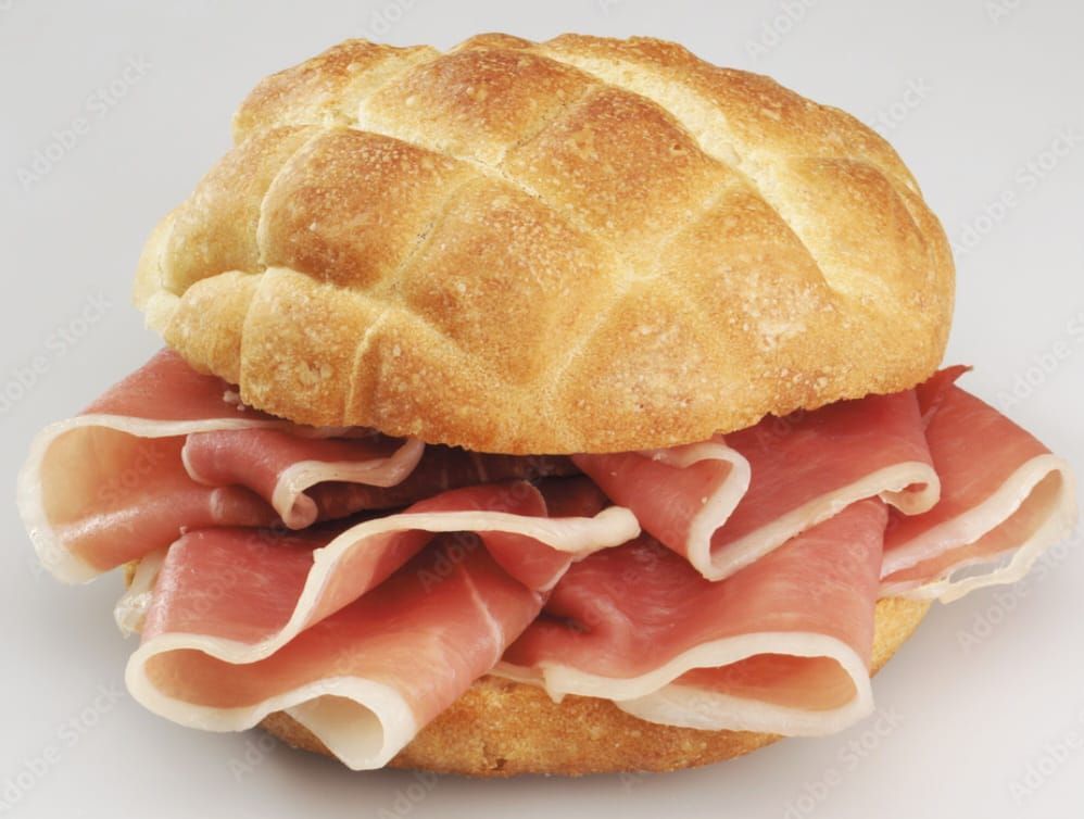 Panino al prosciutto su un panino rotondo decorato con strati sovrapposti di carne rosa.