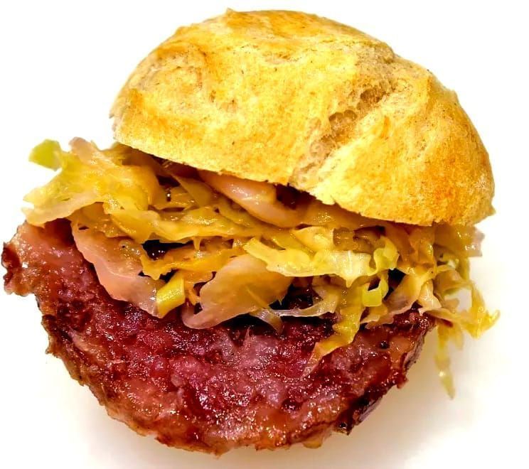 Panino con polpetta di carne rossa fritta, guarnita con cavolo cotto, inserita in un panino rotondo.