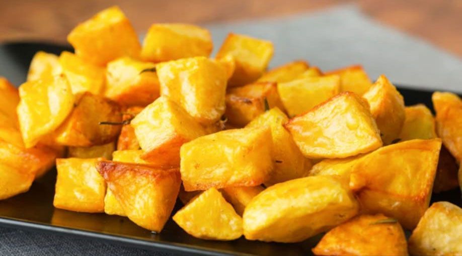 Cubetti di patate dorate e arrostite su un piatto da portata nero.