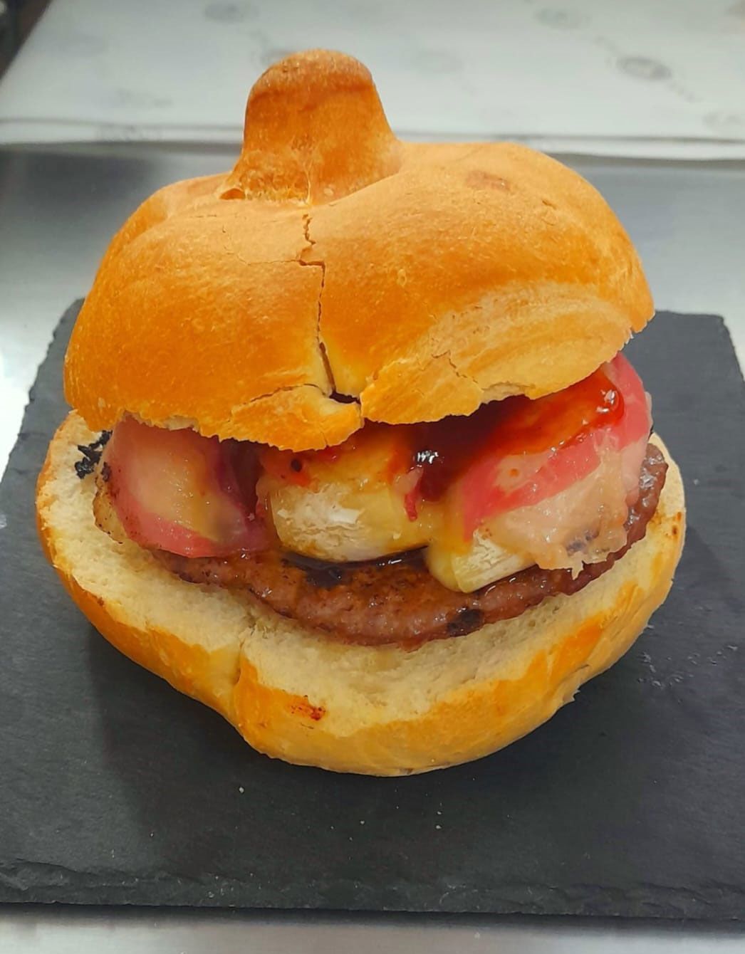 Hamburger con panino, polpetta di carne, formaggio e salsa rossa su una superficie nera.