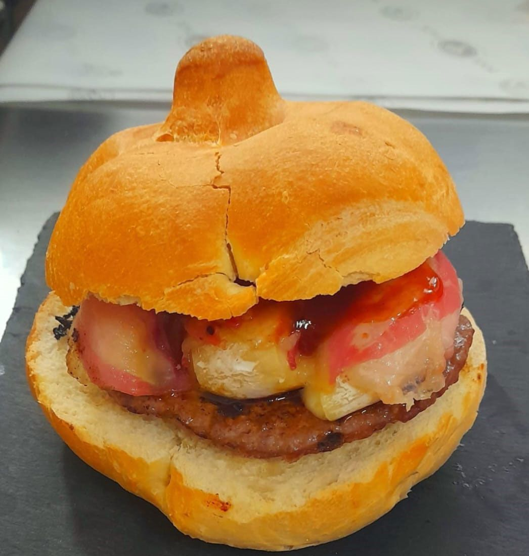 Hamburger con panino rotondo e soffice, polpetta di carne e condimenti, servito su un piatto di ardesia.