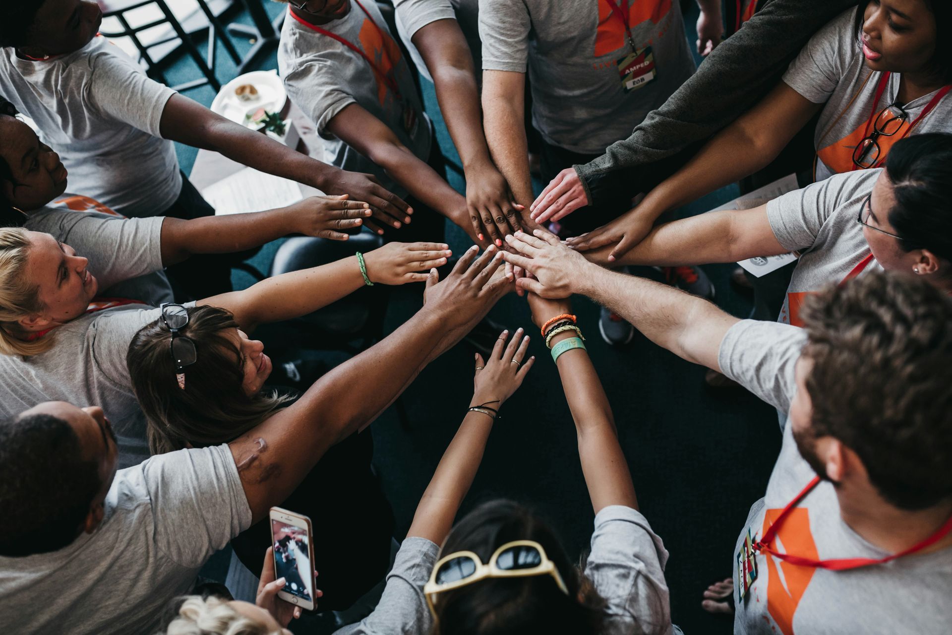 A group of people wearing matching gray T-shirts stand in a circle and place their hands together in the center.