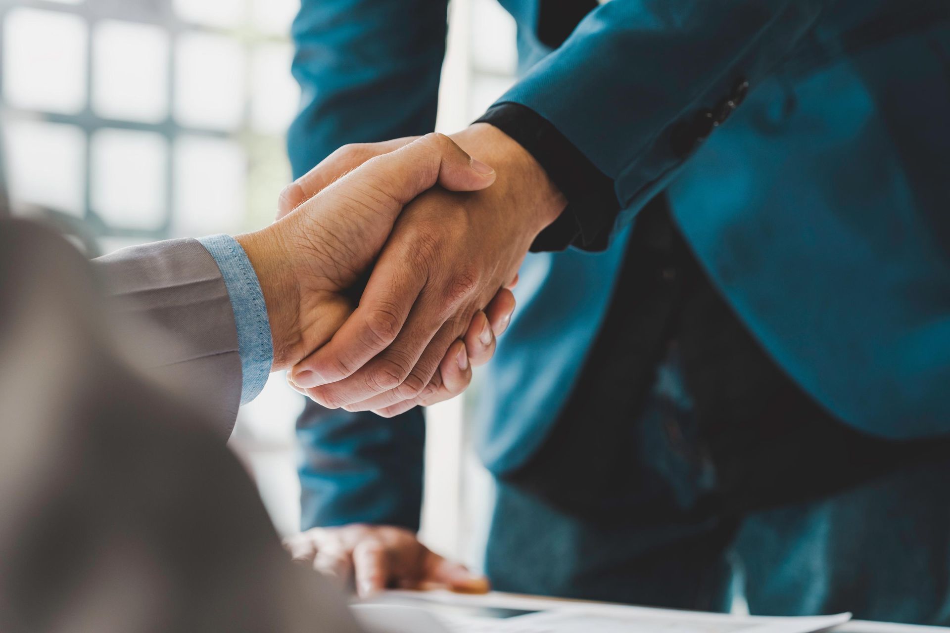 Two people shaking hands in a business meeting, one wearing a blue suit.