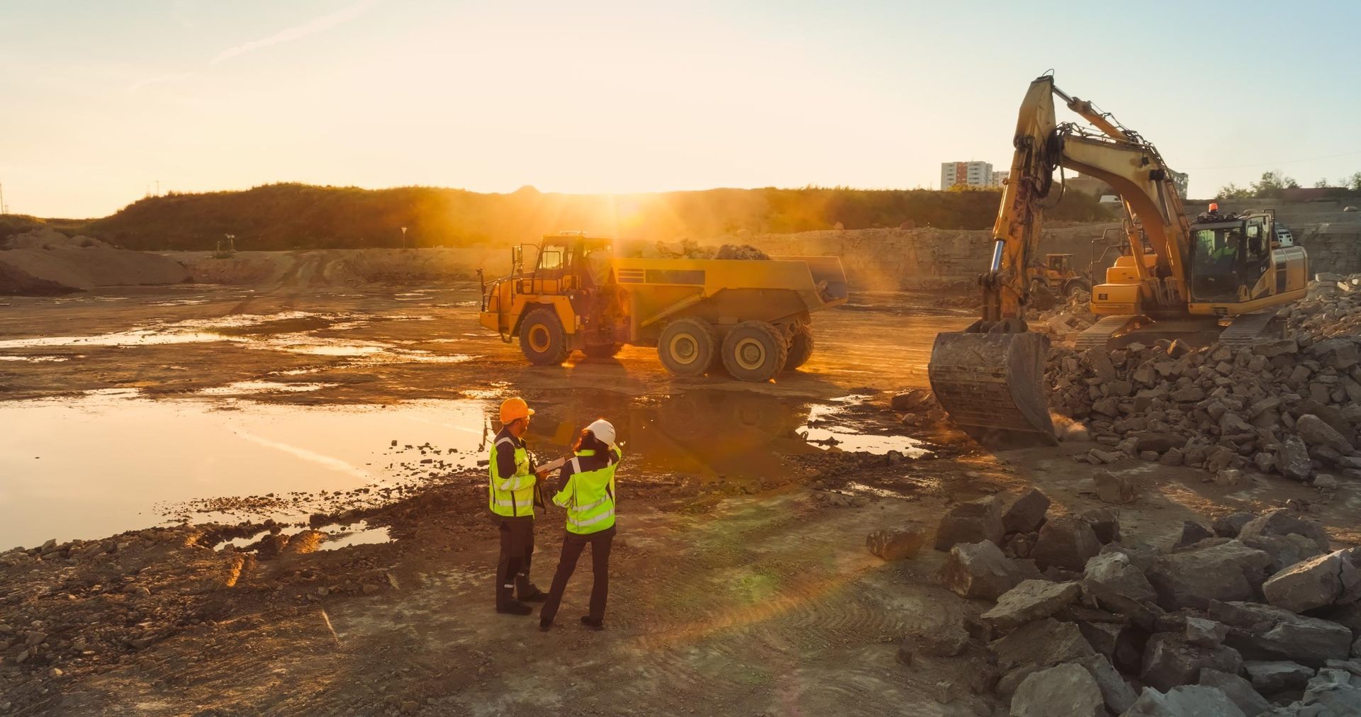 Workers and heavy machinery at a rocky construction site at sunset