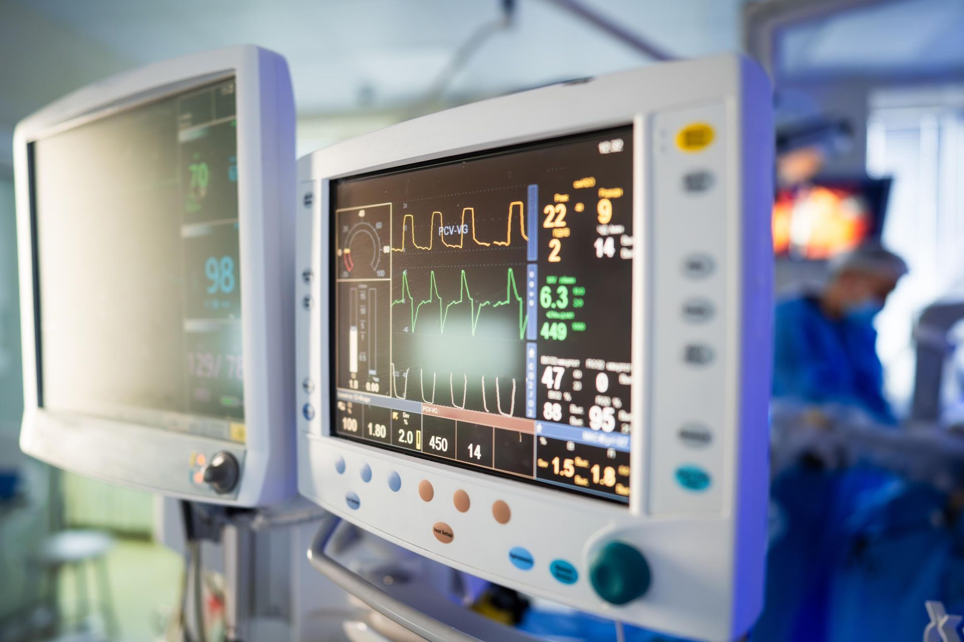 Hospital monitor displaying vital signs beside a patient bed in a clinical setting