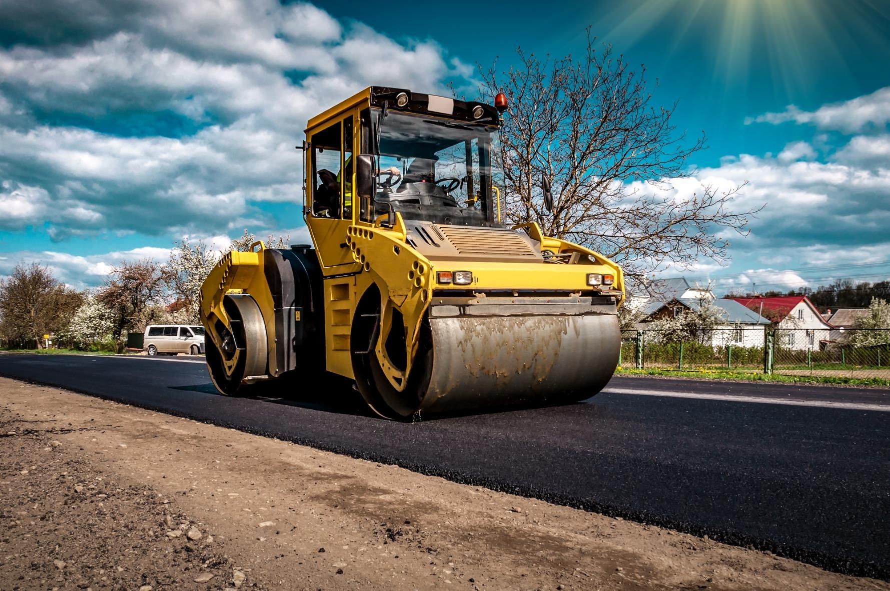 Yellow road roller paving a freshly laid black road under a bright blue sky