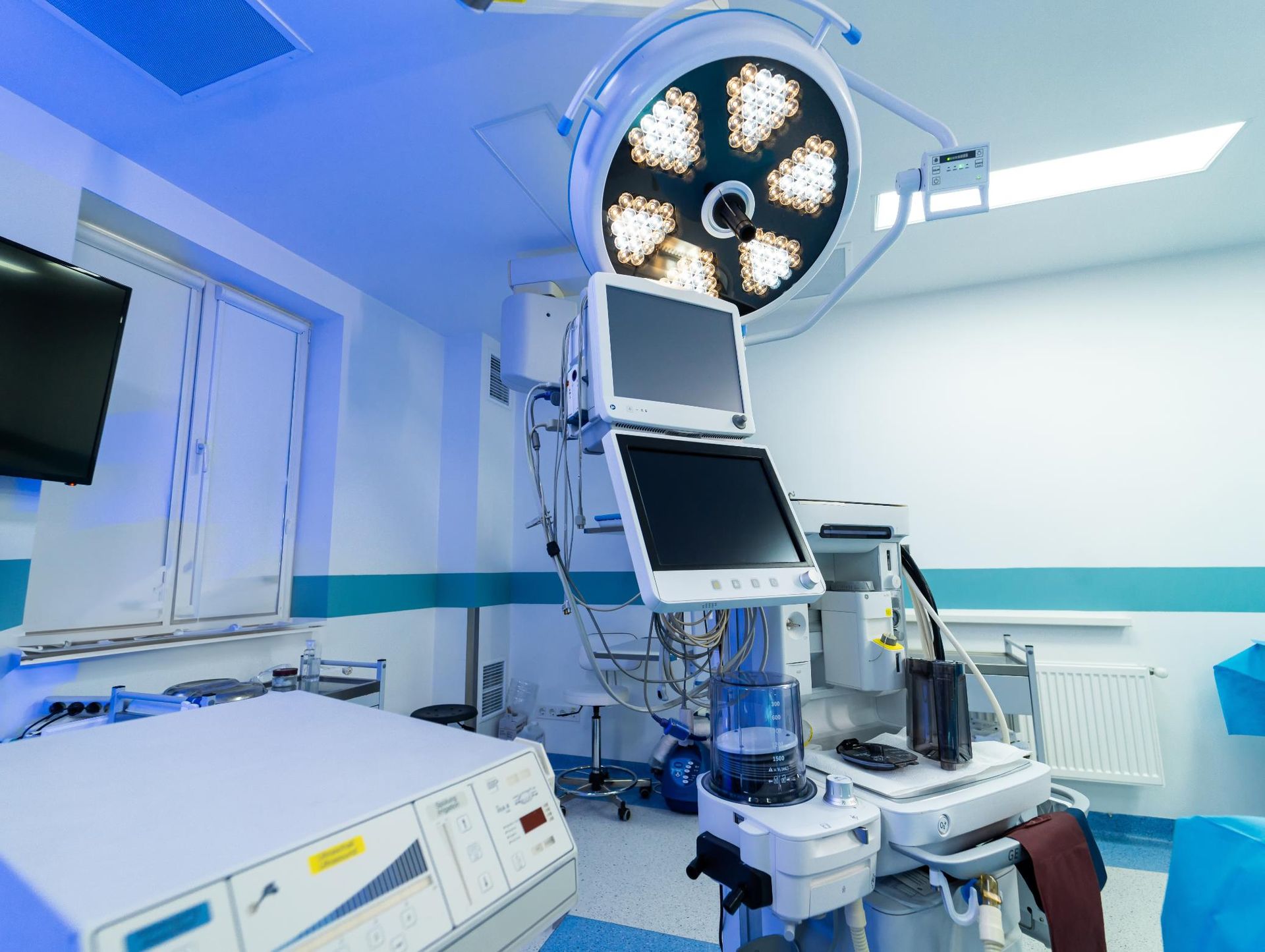 Operating room with surgical equipment and overhead lights in a clean, blue-lit hospital setting
