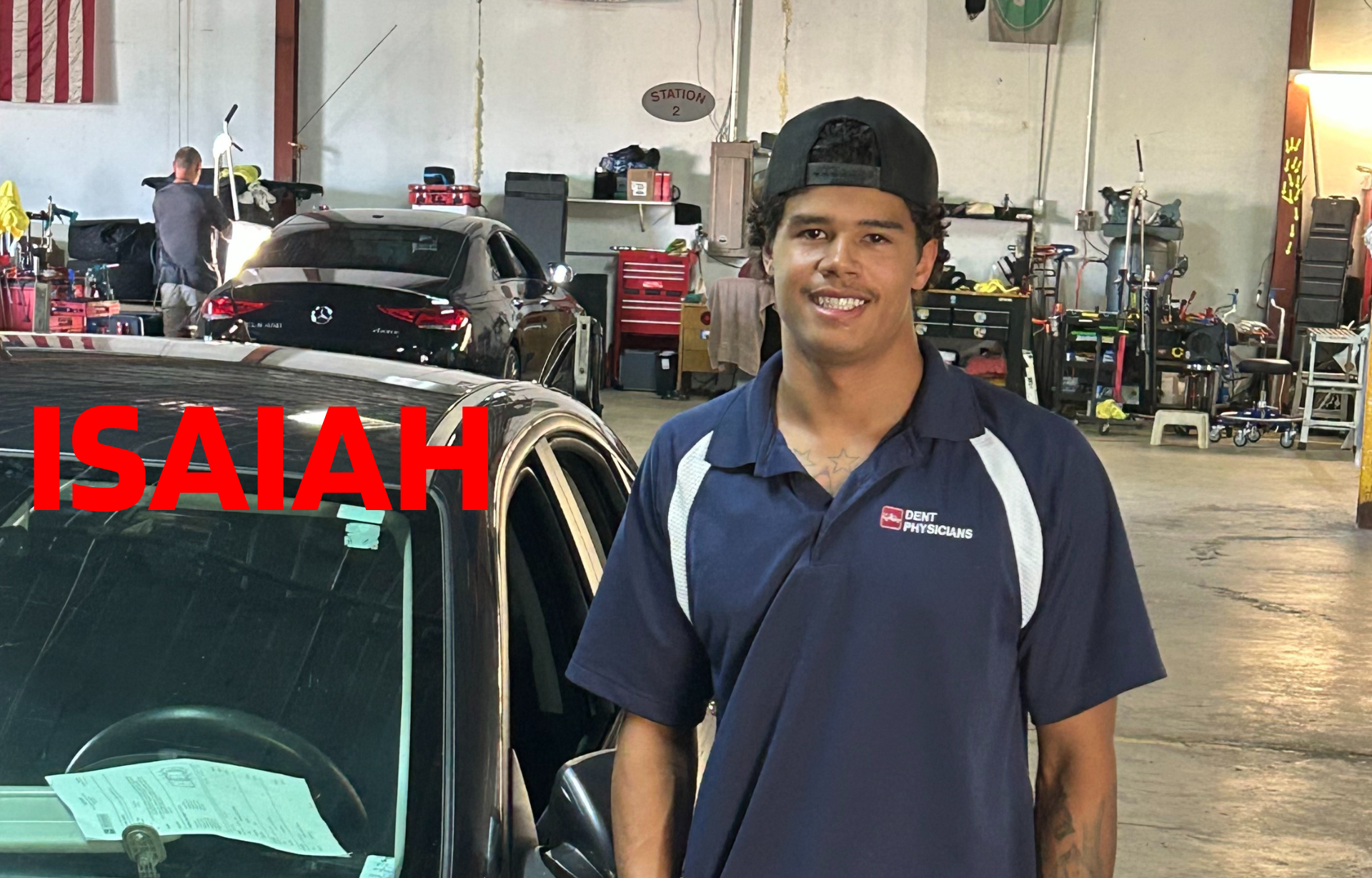 Man in blue shirt stands next to black car; red letters spell