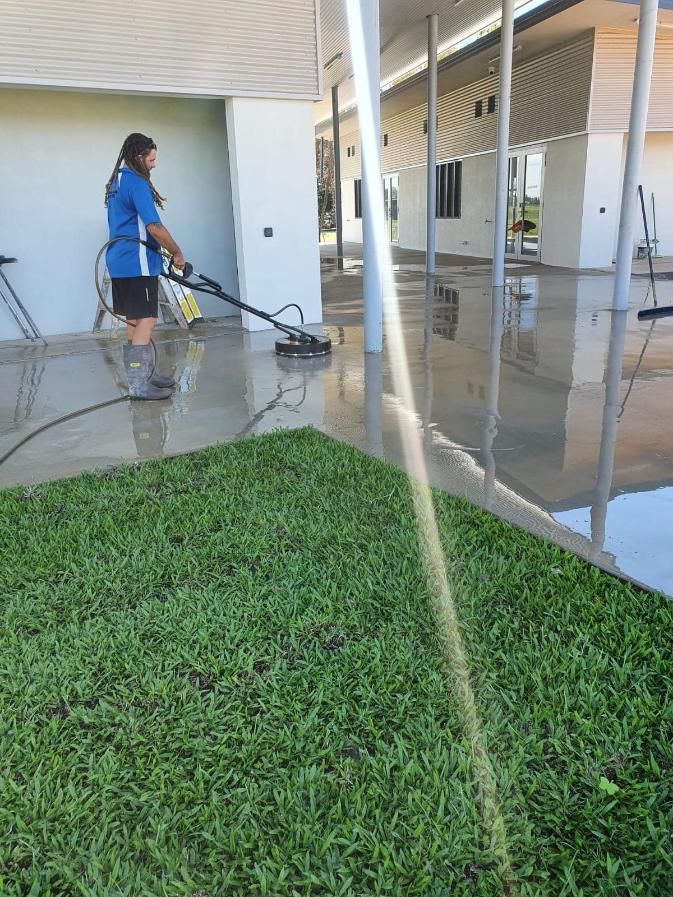 A Man is Using a Pressure Washer to Clean a Concrete Sidewalk — Bark Concreting In Ryan, QLD