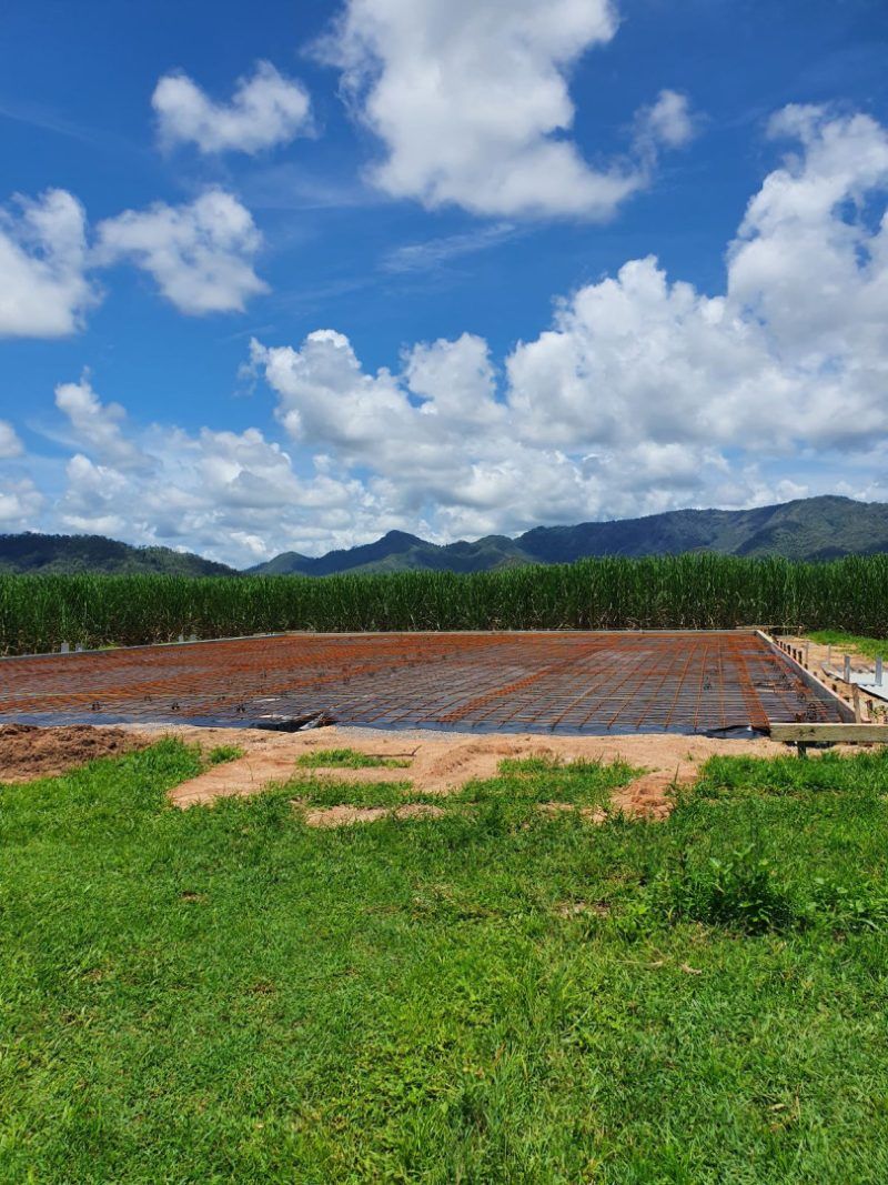 A Large Field Of Grass And Dirt With Mountains In The Background On A Sunny Day — Bark Concreting In Ryan, QLD