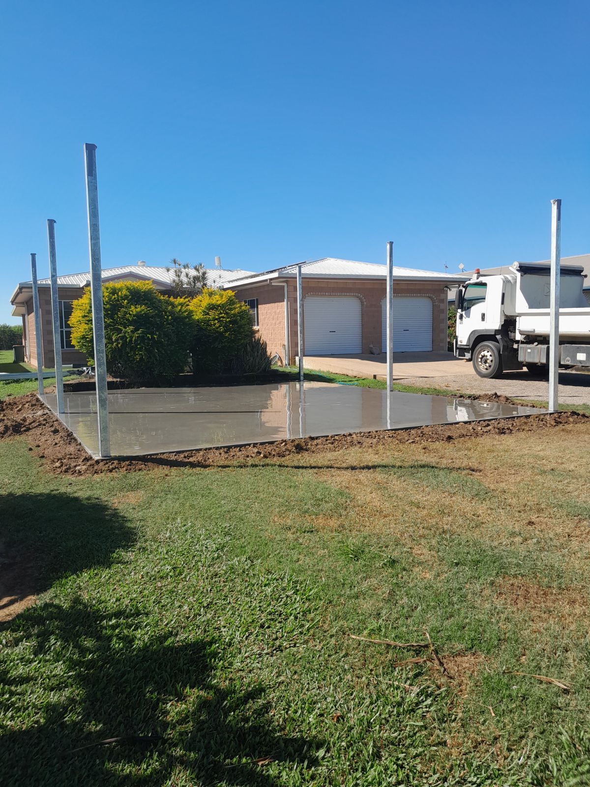 A Concrete Patio With poles around it  is Being Built on the Side of a House — Bark Concreting In Ryan, QLD