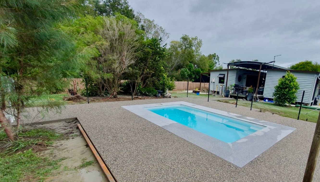 A Beach Ball is Sitting on the Grass in Front of a Pool — Bark Concreting In Ryan, QLD