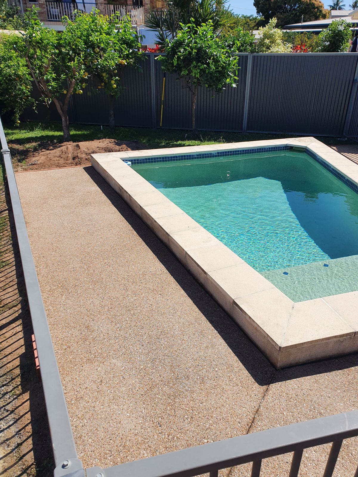 A Swimming Pool Is Surrounded By A Fence And Trees In A Backyard — Bark Concreting In Ryan, QLD