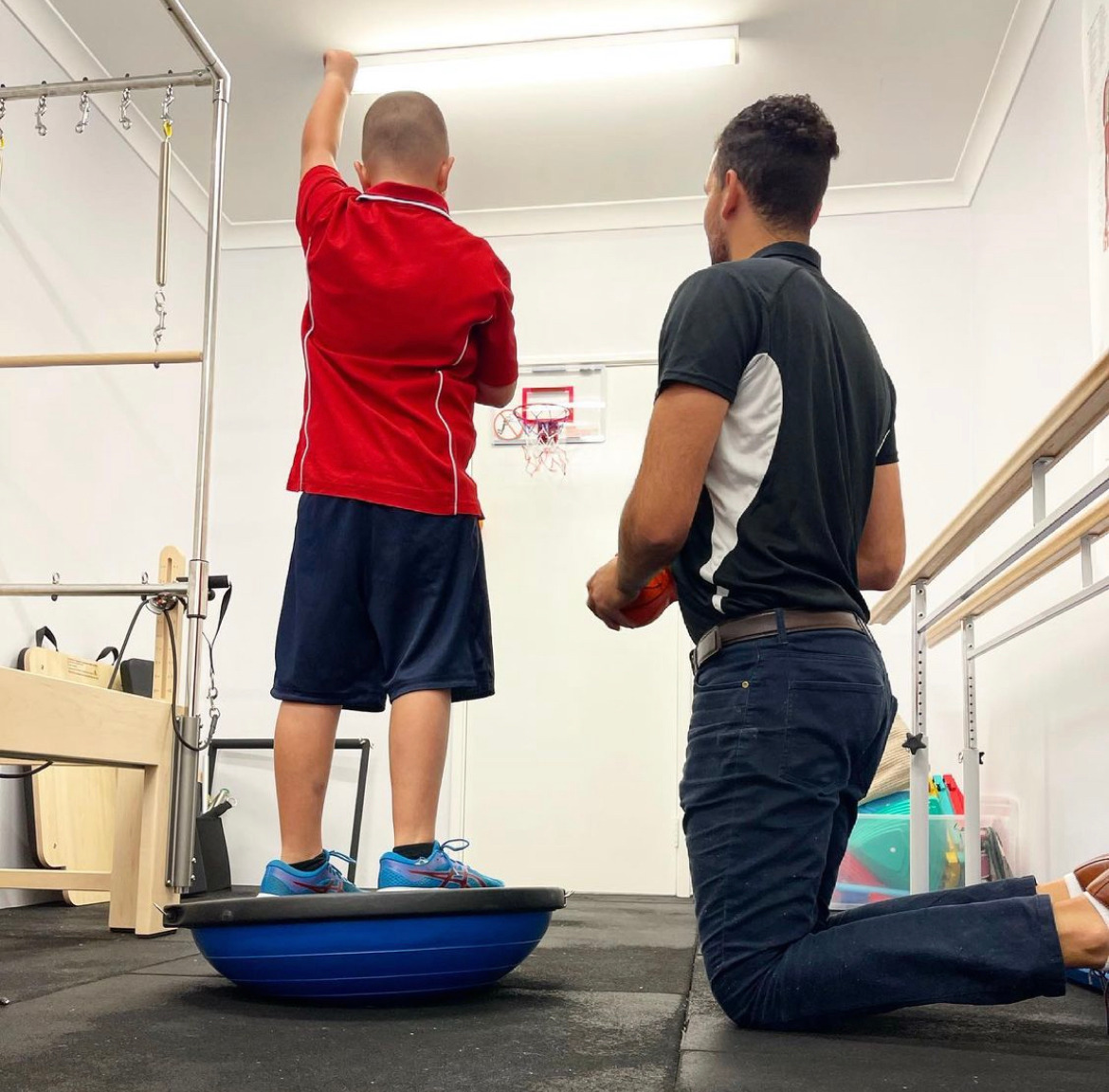 A boy in a red shirt is standing on a blue balance ball
