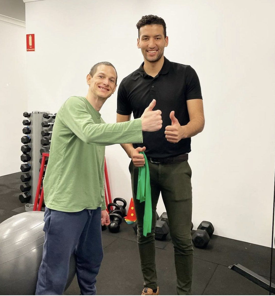 Two men are giving a thumbs up in a gym