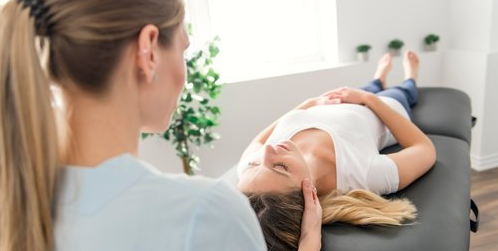 A woman is laying on a table getting a head massage.