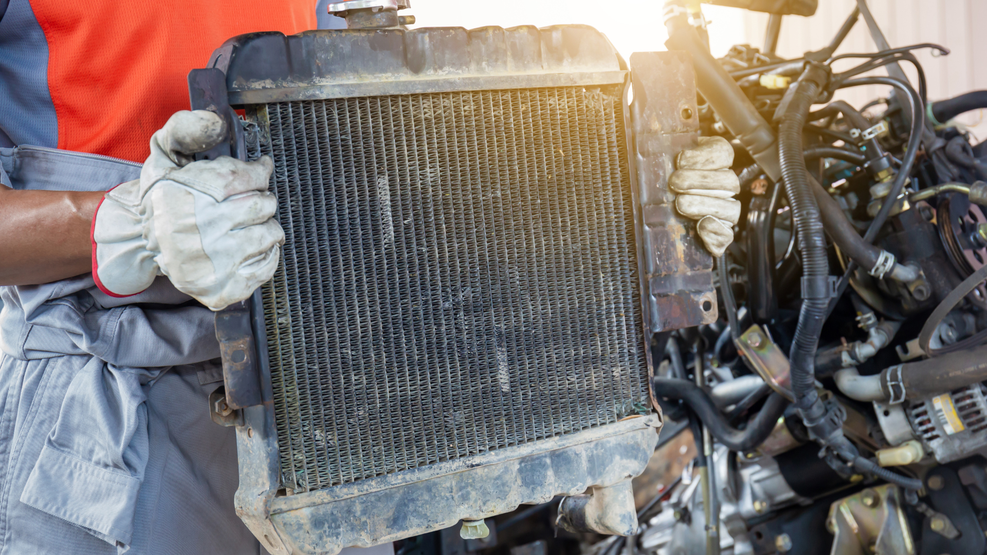 A man is holding a radiator in front of a car engine.