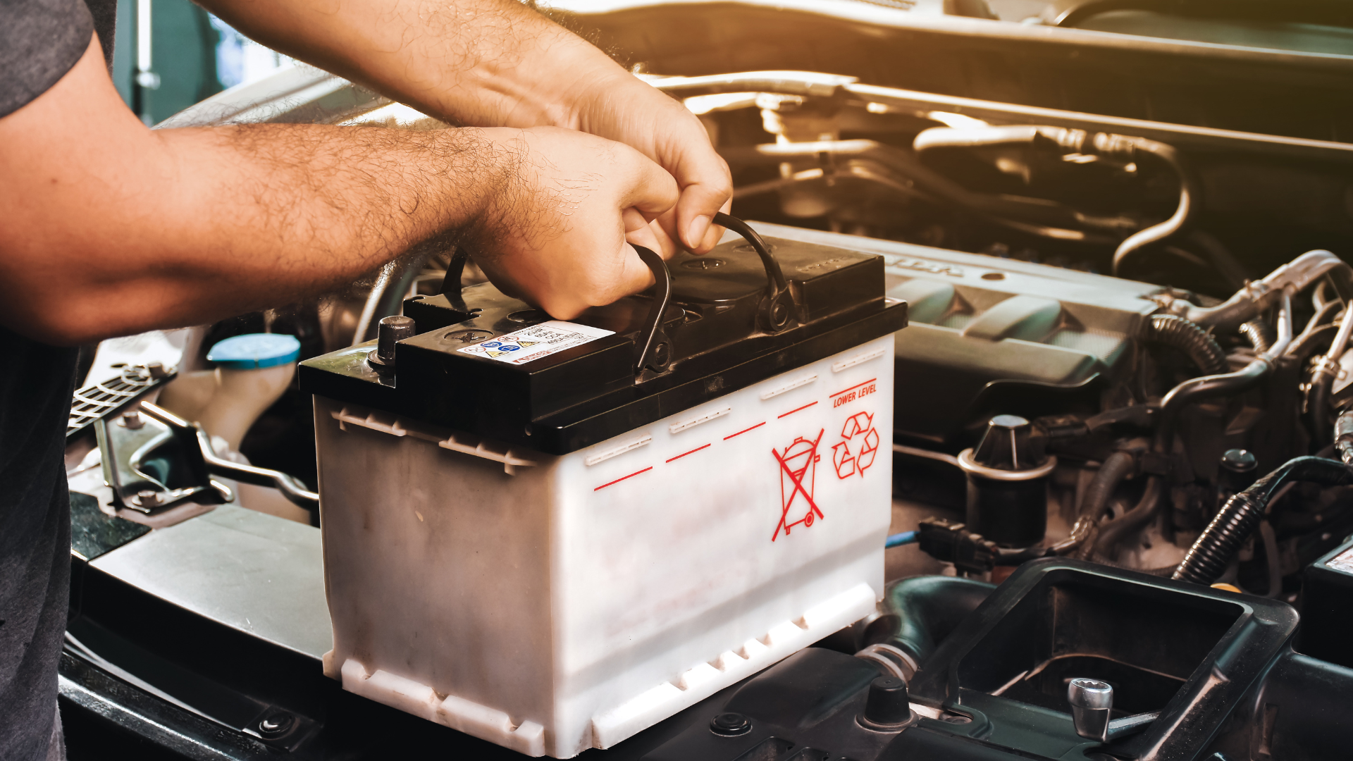 A man is fixing a car battery in a garage.