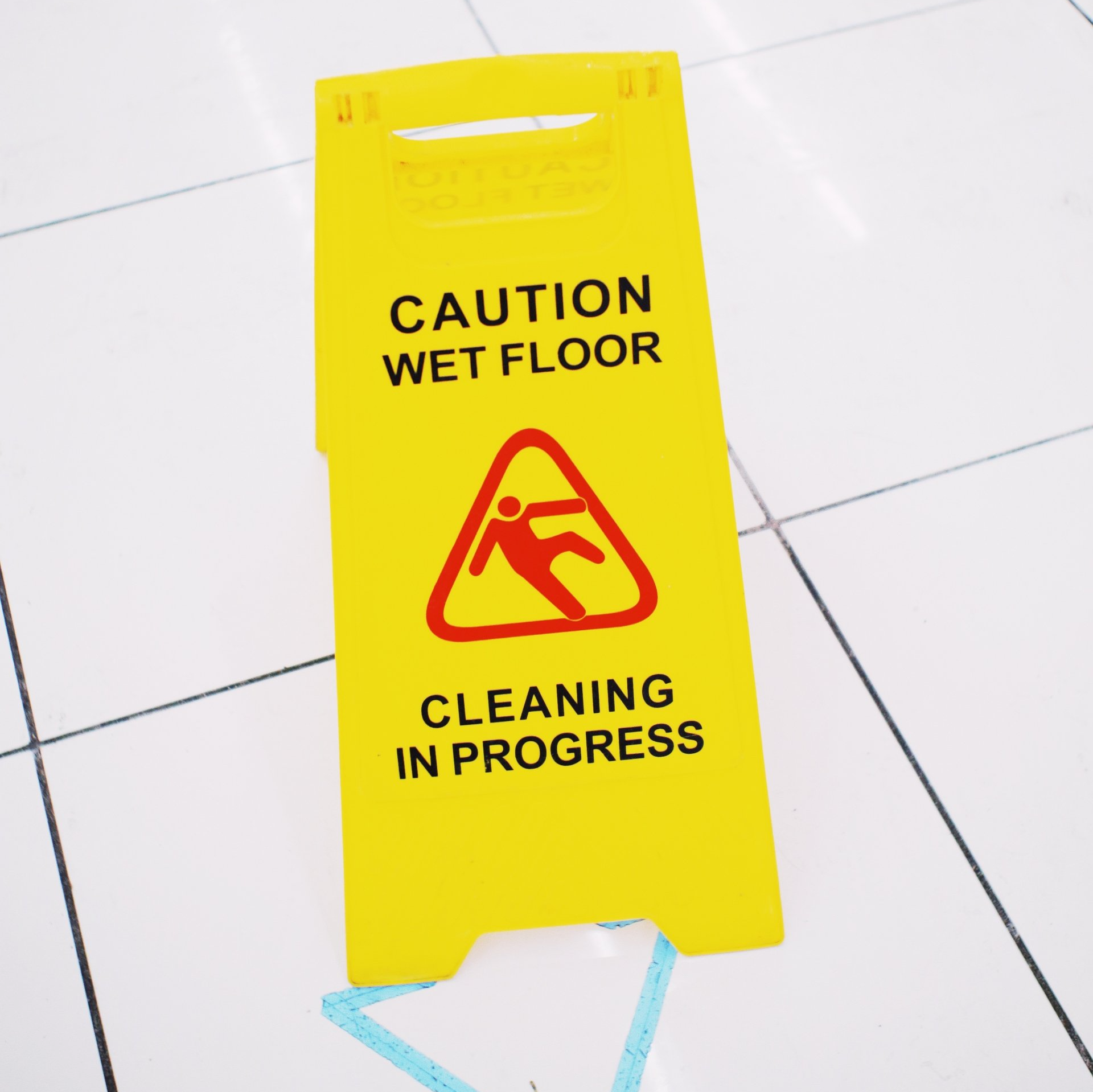 Yellow caution wet floor sign on tiled floor, reading “Cleaning in Progress.”