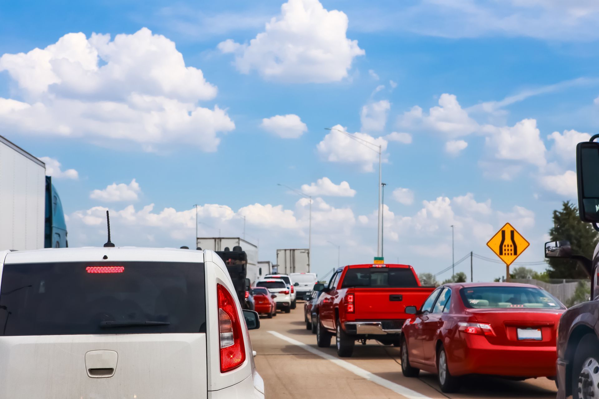 Traffic jam on a highway with cars and trucks under a bright blue sky.