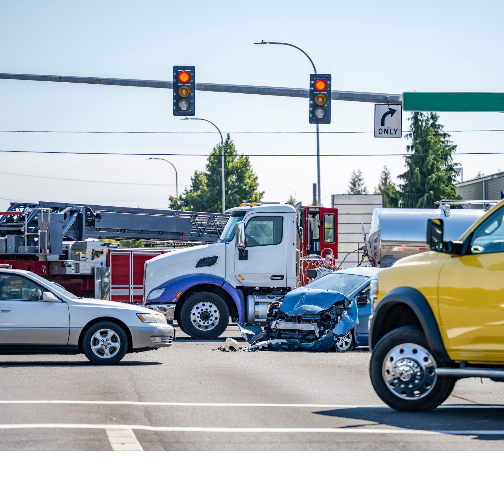 Traffic collision at an intersection with a blue car crushed between a white truck and a yellow pickup.