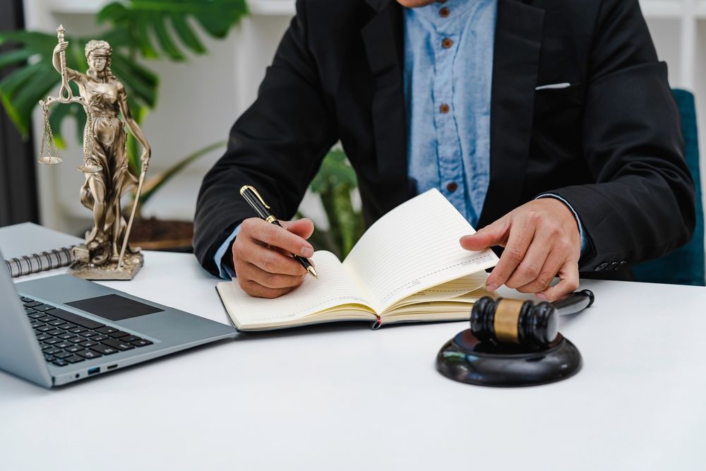 Lawyer writing in a notebook at a desk with a laptop, gavel, and gold justice statue