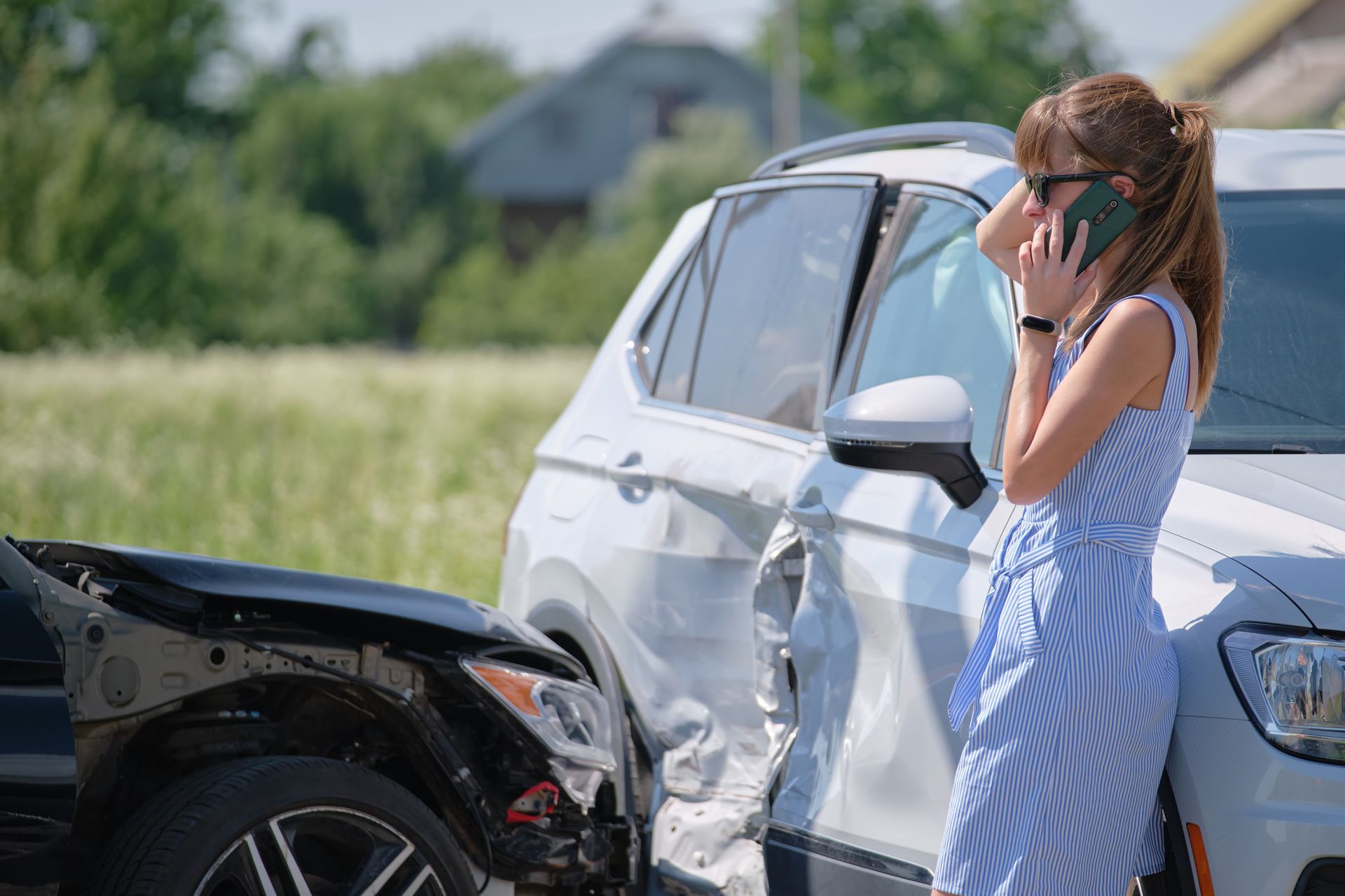Woman standing by a white car after a collision with a black car in a grassy field